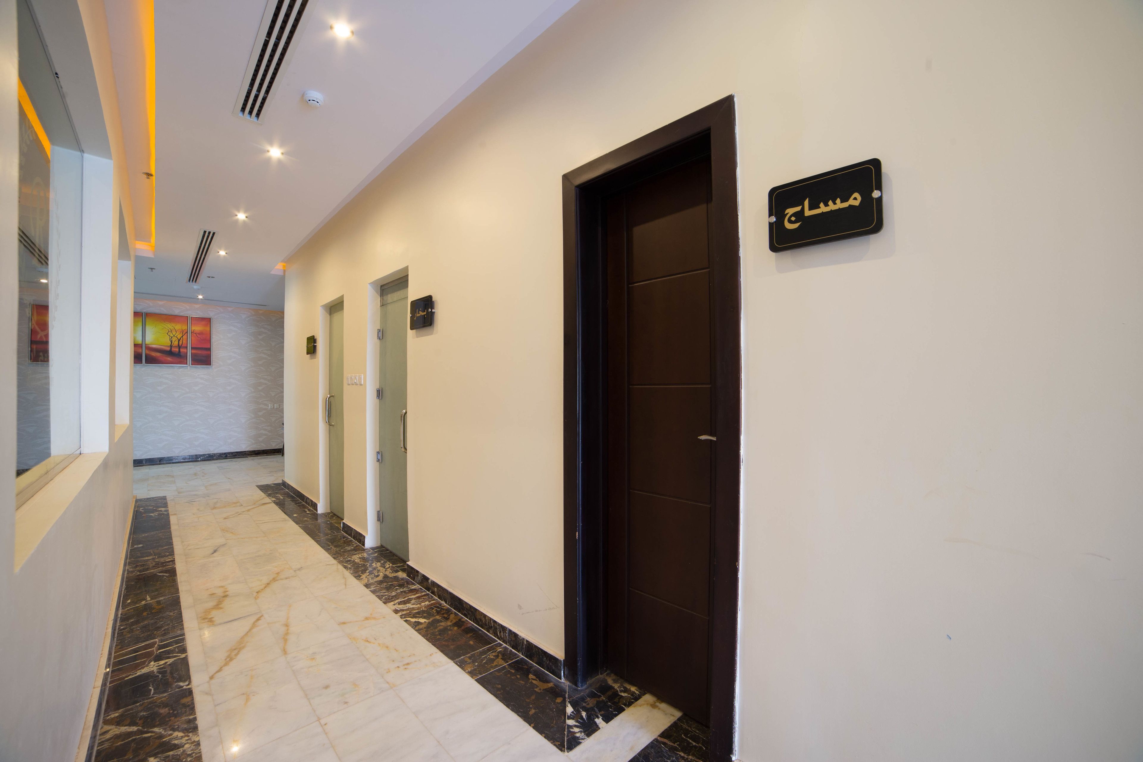A hotel hallway with a marble floor, a door with a sign, and a painting on the wall.