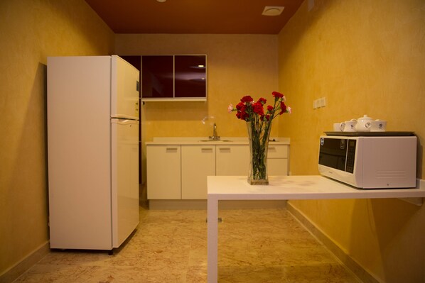 A compact kitchen with a refrigerator, microwave, and a vase with flowers on a table.