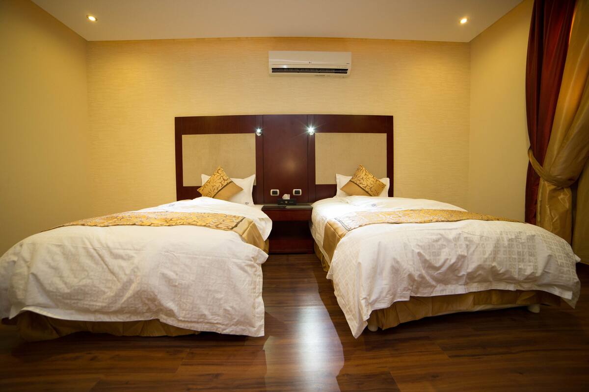 Ein Hotelzimmer mit zwei Betten, einem großen Spiegel, einer Klimaanlage und Holzboden.