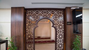A reception area with a wooden decorative screen, a flat-screen TV, and two potted plants. - Raoum Inn Hotel Apartments- Buraydah (Buraydah)