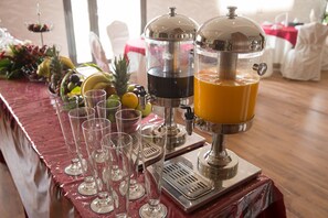 A juice bar with multiple dispensers and glasses on a table, surrounded by fruits and a decorative centerpiece.