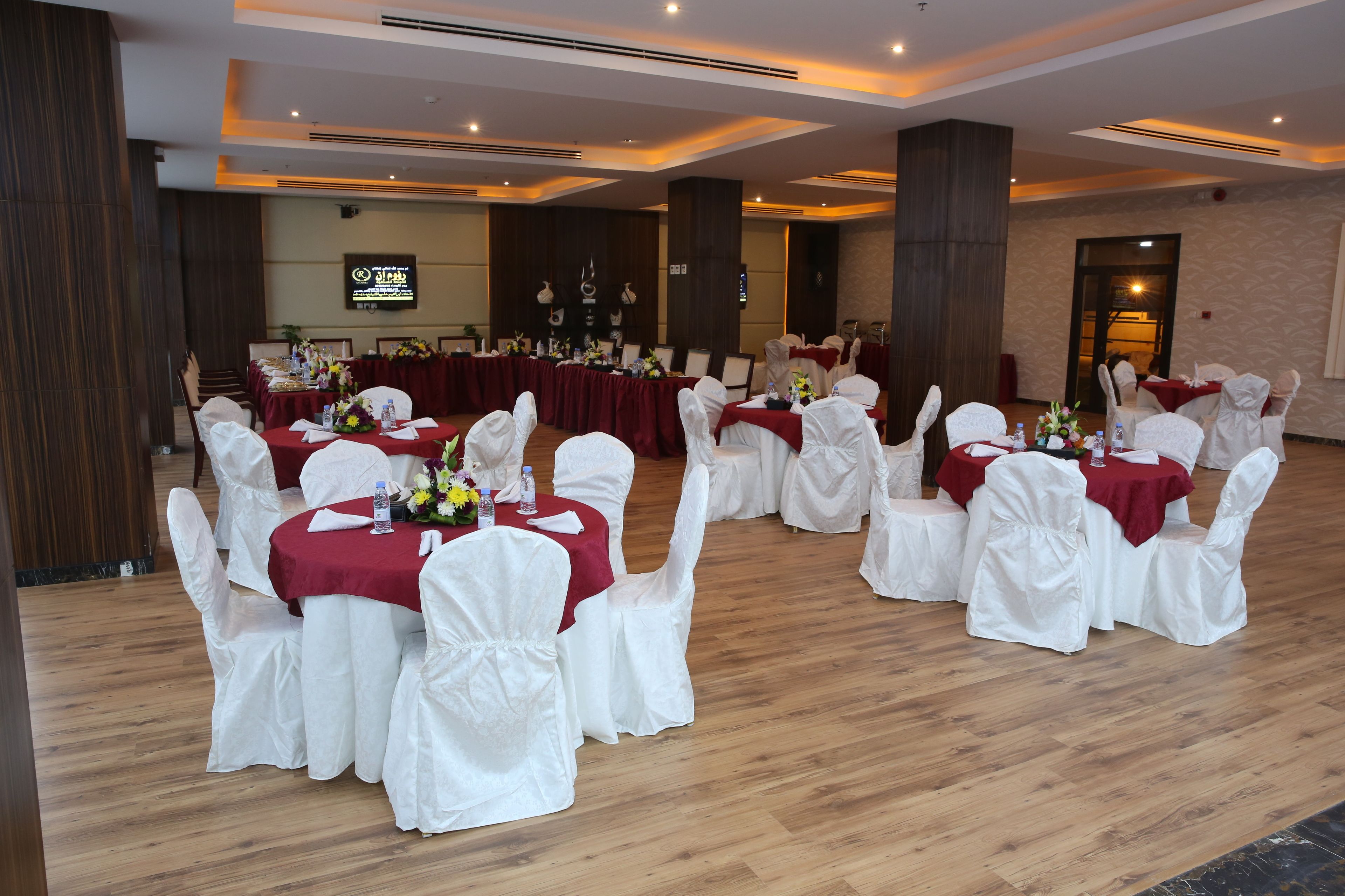 A banquet hall with round tables covered in red tablecloths and white chair covers, arranged in a semi-circle.