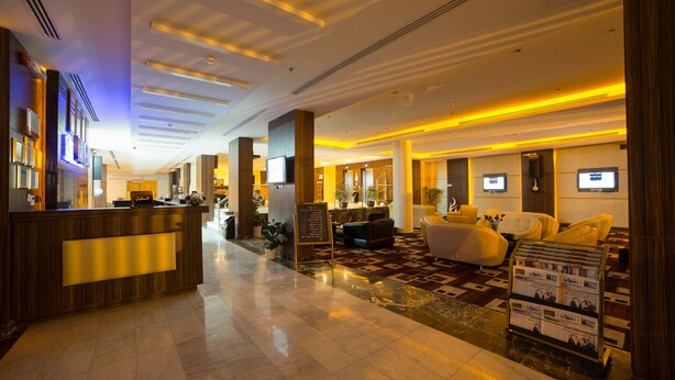 A hotel lobby with a reception desk, seating area, and a digital information board. - Raoum Inn Hotel Apartments- Buraydah (Buraydah)