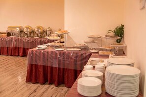 A buffet setup with multiple serving stations, covered tables, and stacked plates.