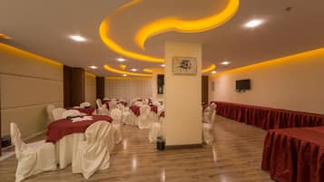 Una sala de banquets amb taules rodones cobertes amb mantells vermells, cadires blanques i un pilar central amb una obra d'art emmarcada.