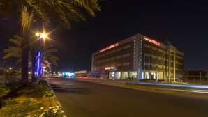 Un bâtiment moderne avec une enseigne lumineuse, une rue bien éclairée et des palmiers.
