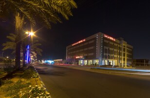A modern building with illuminated signage, a well-lit street, and palm trees.