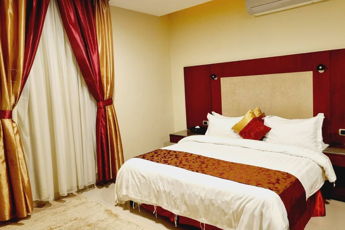 A hotel room with a large bed, a red headboard, and a red and white curtain.