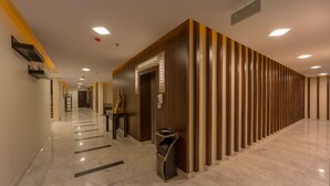 Un couloir d’hôtel avec un sol en marbre, un lambris en bois d’un côté et un comptoir de réception avec une poubelle.
