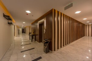 A hotel corridor with a marble floor, wooden paneling on one side, and a reception desk with a trash bin.