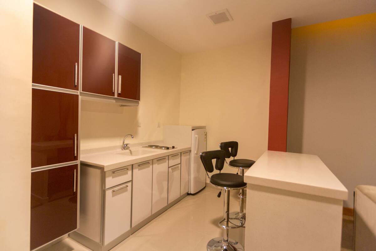 A compact kitchen with a white countertop, stainless steel appliances, and a bar stool.