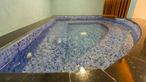 Un petit bain à remous carré, avec des carreaux de mosaïque bleus et un fond noir.