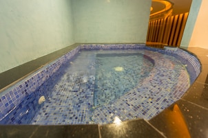 A small, square hot tub with blue mosaic tiles and a black floor.