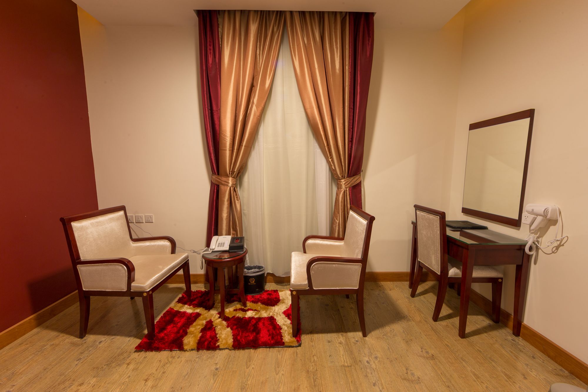 A hotel room with two chairs, a small table, a desk with a mirror, a telephone, and a hairdryer.