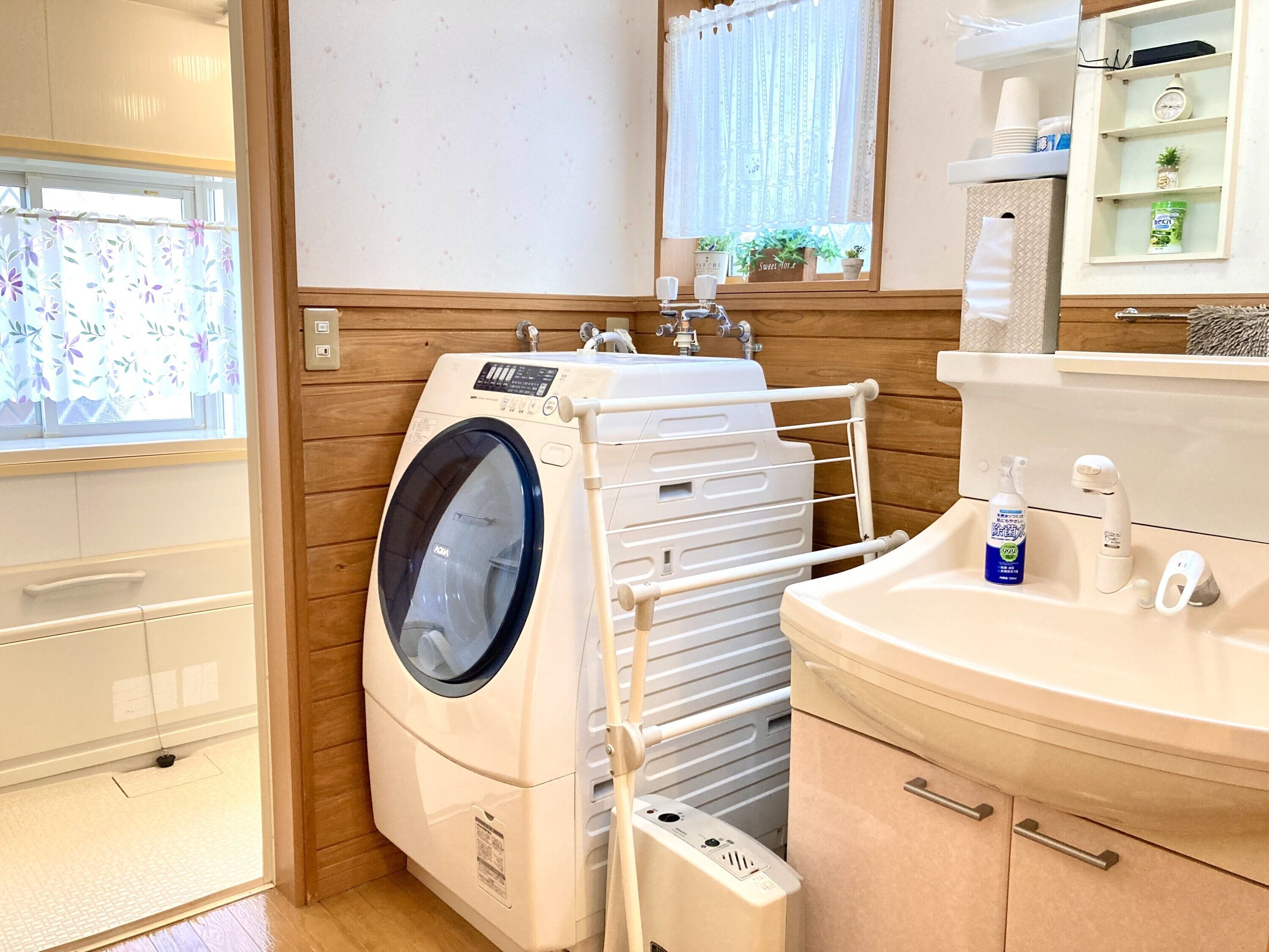 A laundry area with a front-loading washing machine, a drying rack, and a sink with a bottle of hand soap.