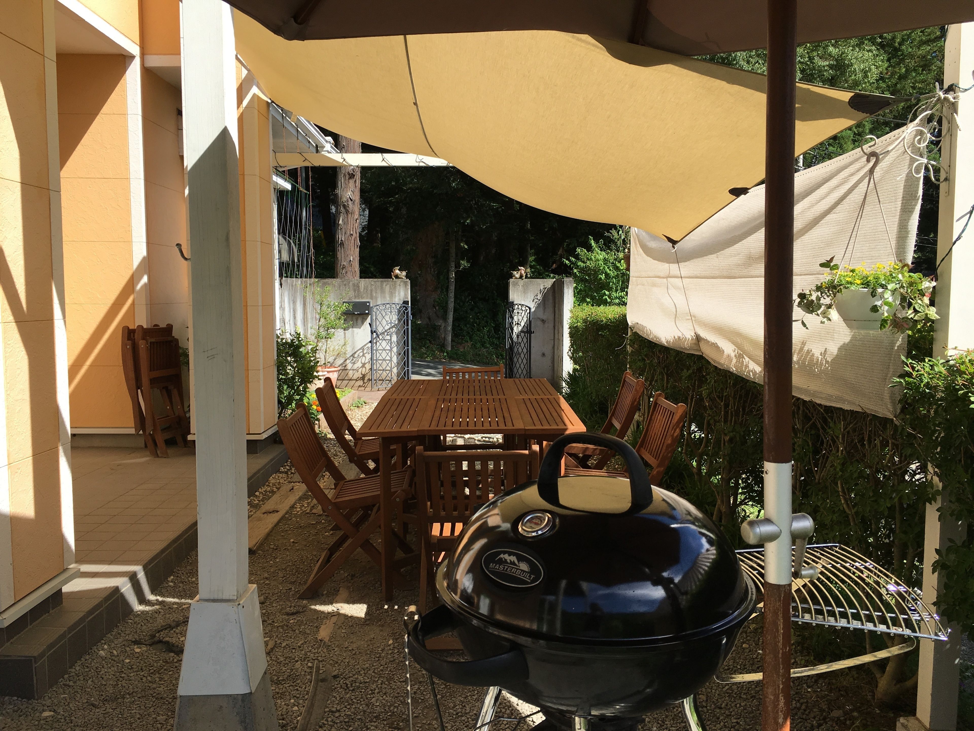 An outdoor patio with a wooden table and chairs, a barbecue grill, and a covered area with a hanging plant.