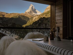 A room with a view of a mountain peak, a wooden interior, and a table with a book and a lamp. - OVERLOOK Lodge by CERVO Zermatt (Zermatt)