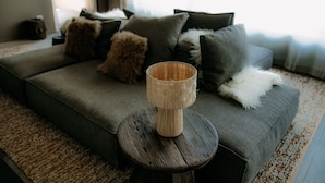 A modern living room with a grey sofa, a round wooden coffee table, and a woven candle holder. - OVERLOOK Lodge by CERVO Zermatt (Zermatt)