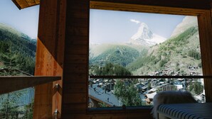 A room with a large window overlooking a mountainous landscape and a village below. - OVERLOOK Lodge by CERVO Zermatt (Zermatt)