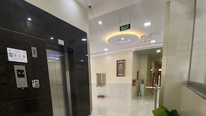 Un hall d’entrée moderne avec un sol en marbre, un ascenseur, un comptoir de réception et une œuvre d’art encadrée au mur.