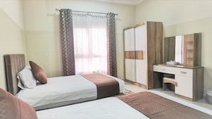 Une chambre avec deux lits, une armoire, un miroir et une fenêtre avec des rideaux.