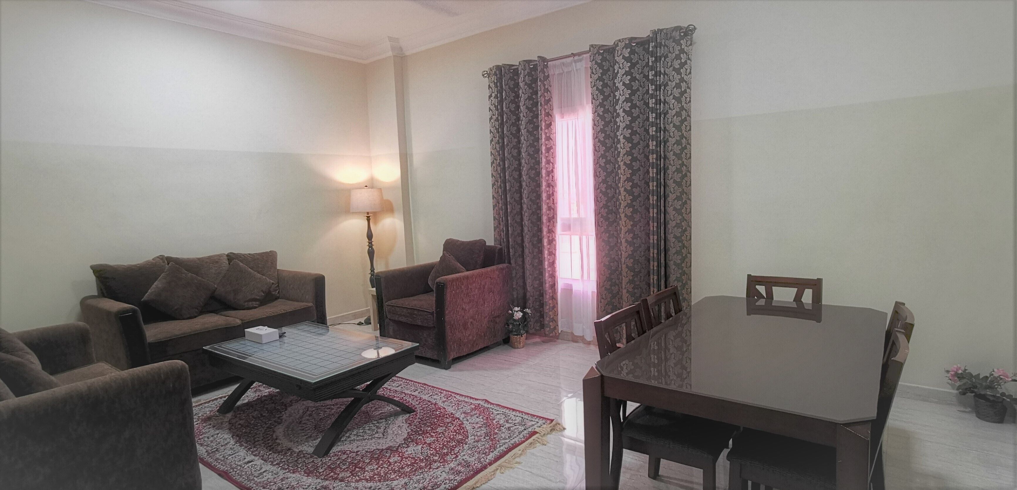 A living room with a sofa set, a coffee table, a dining table with chairs, a lamp, and a window with curtains.