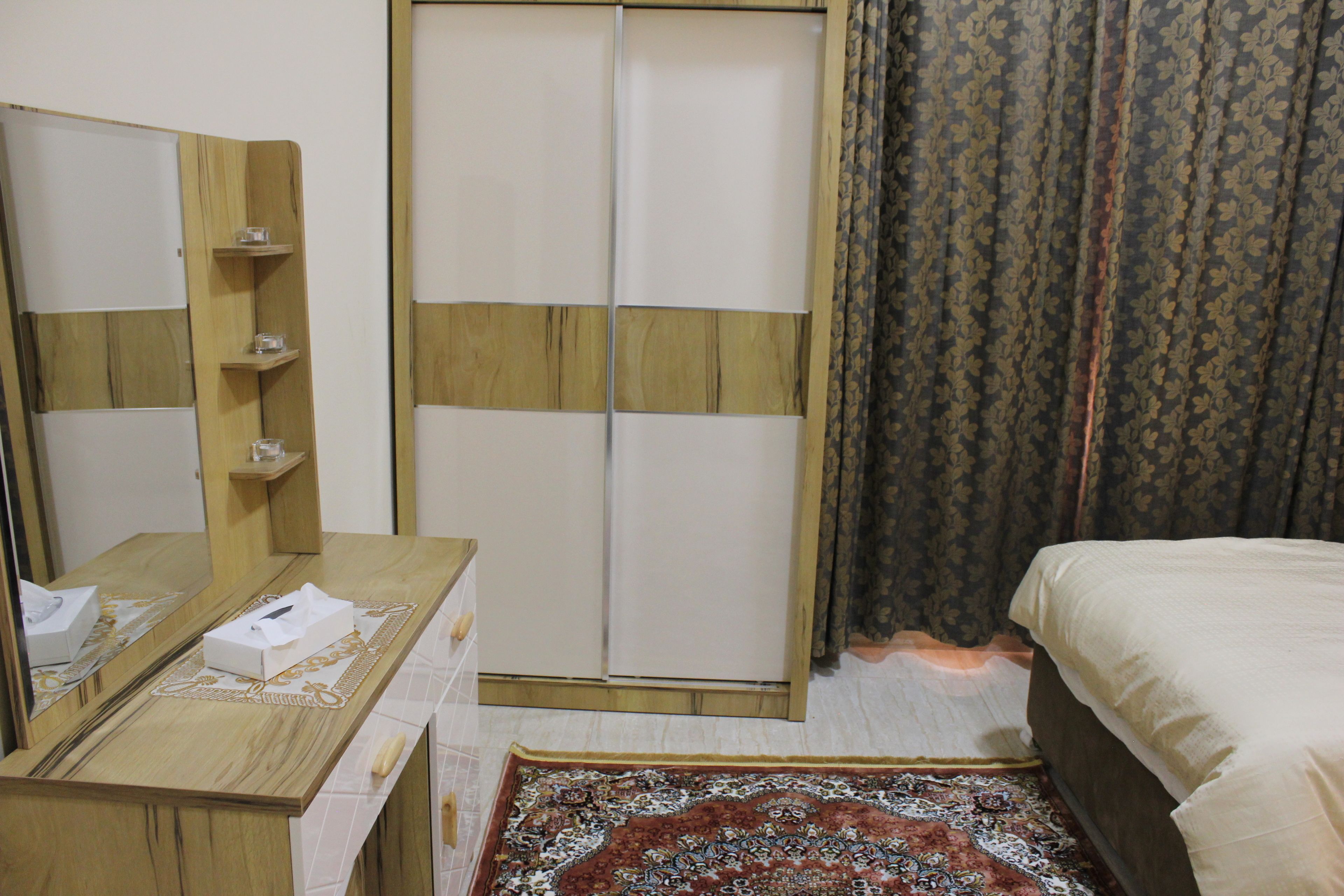 Un dormitorio con un aparador de madera, un espejo, una cama y un tapete estampado.