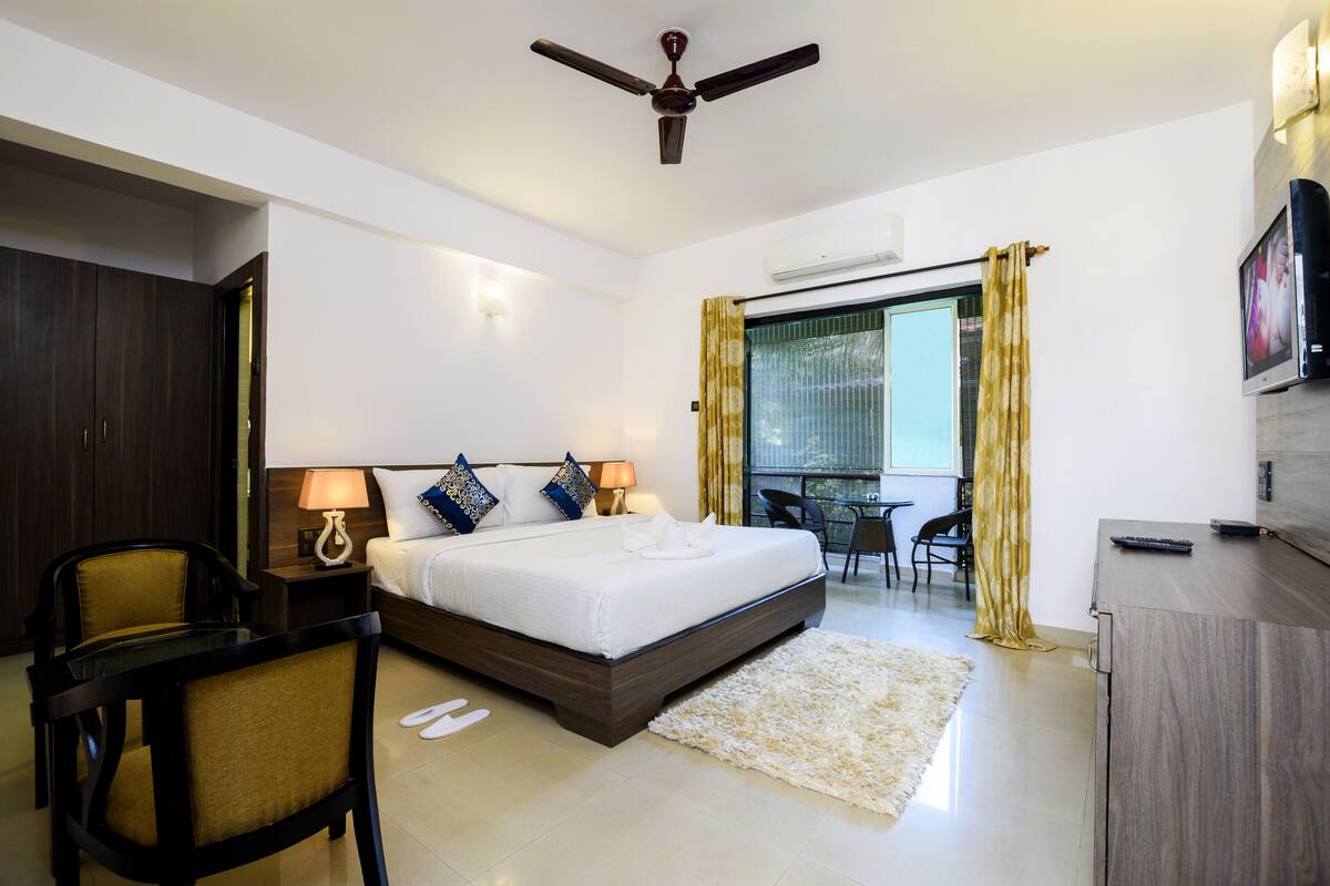 A hotel room with a bed, bedside tables, a desk, a chair, a ceiling fan, and a TV.
