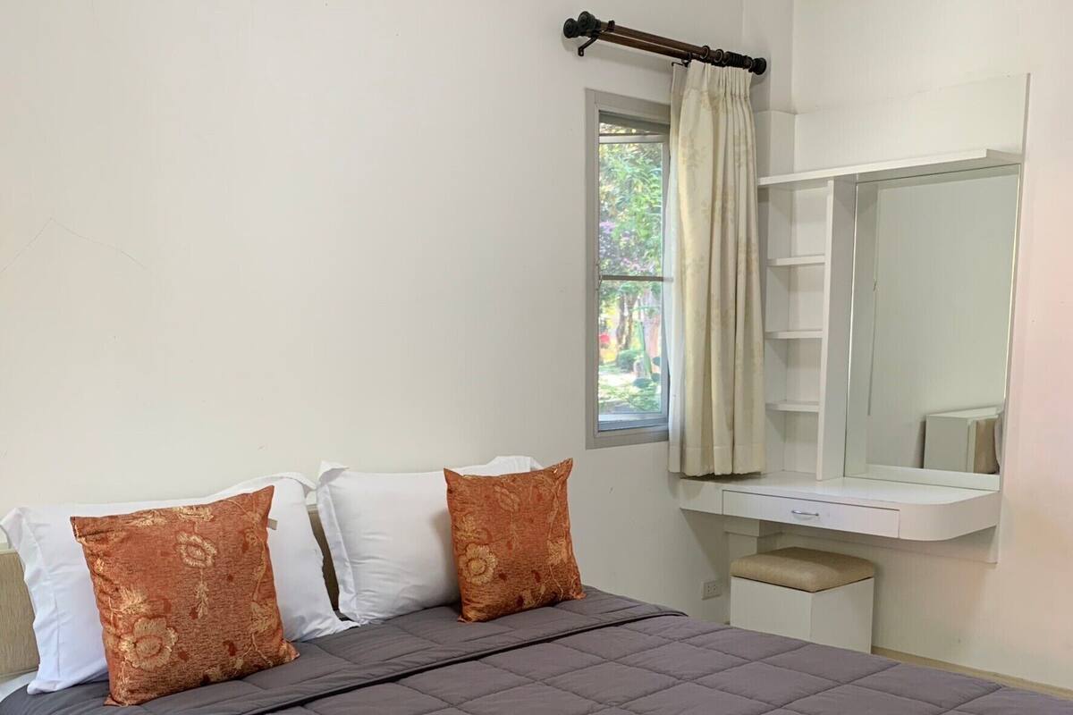 A bedroom with a bed, a window with curtains, a bedside table, and a mirror.