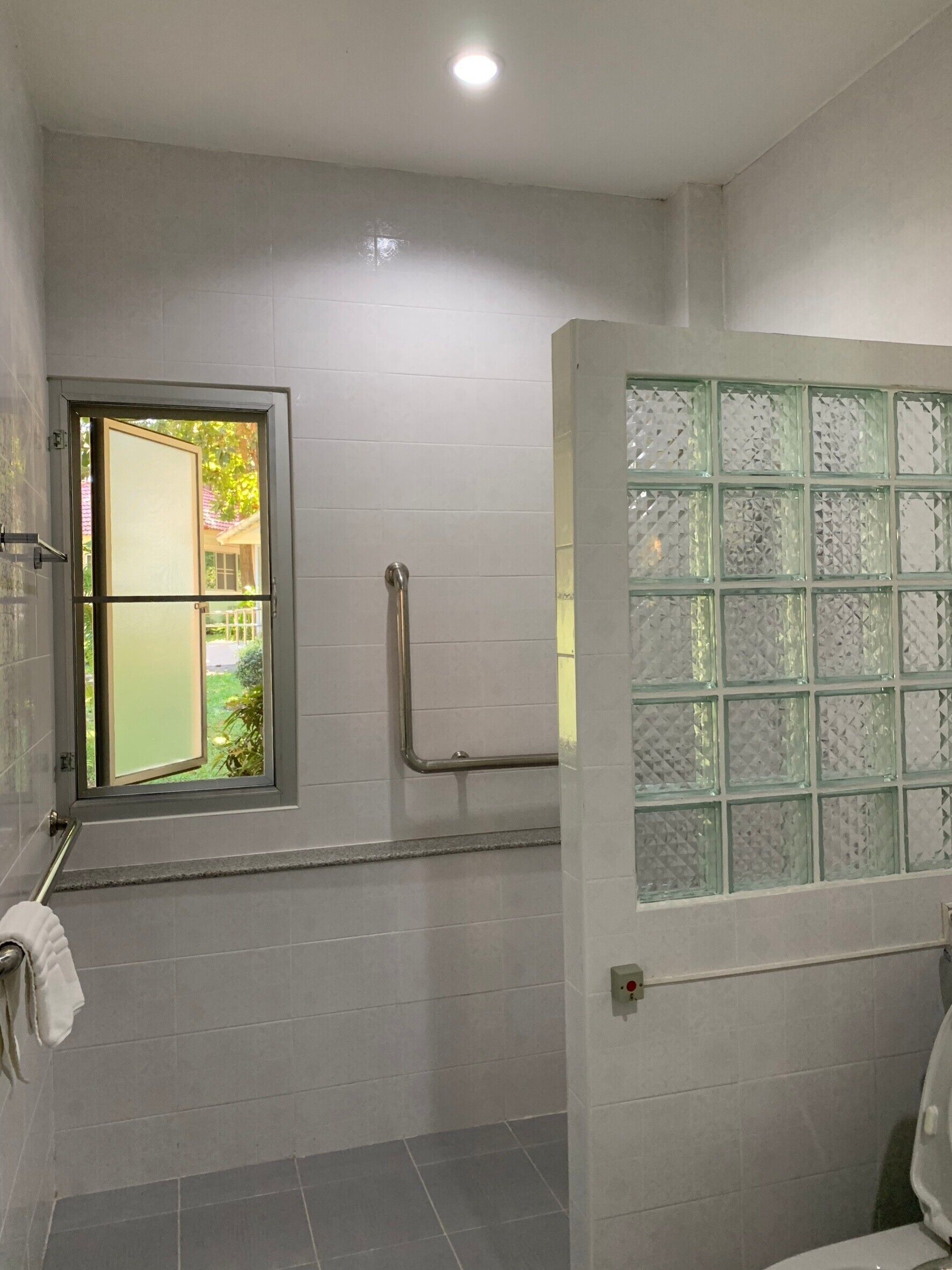 Um banheiro com janela, porta de vidro e corrimão.