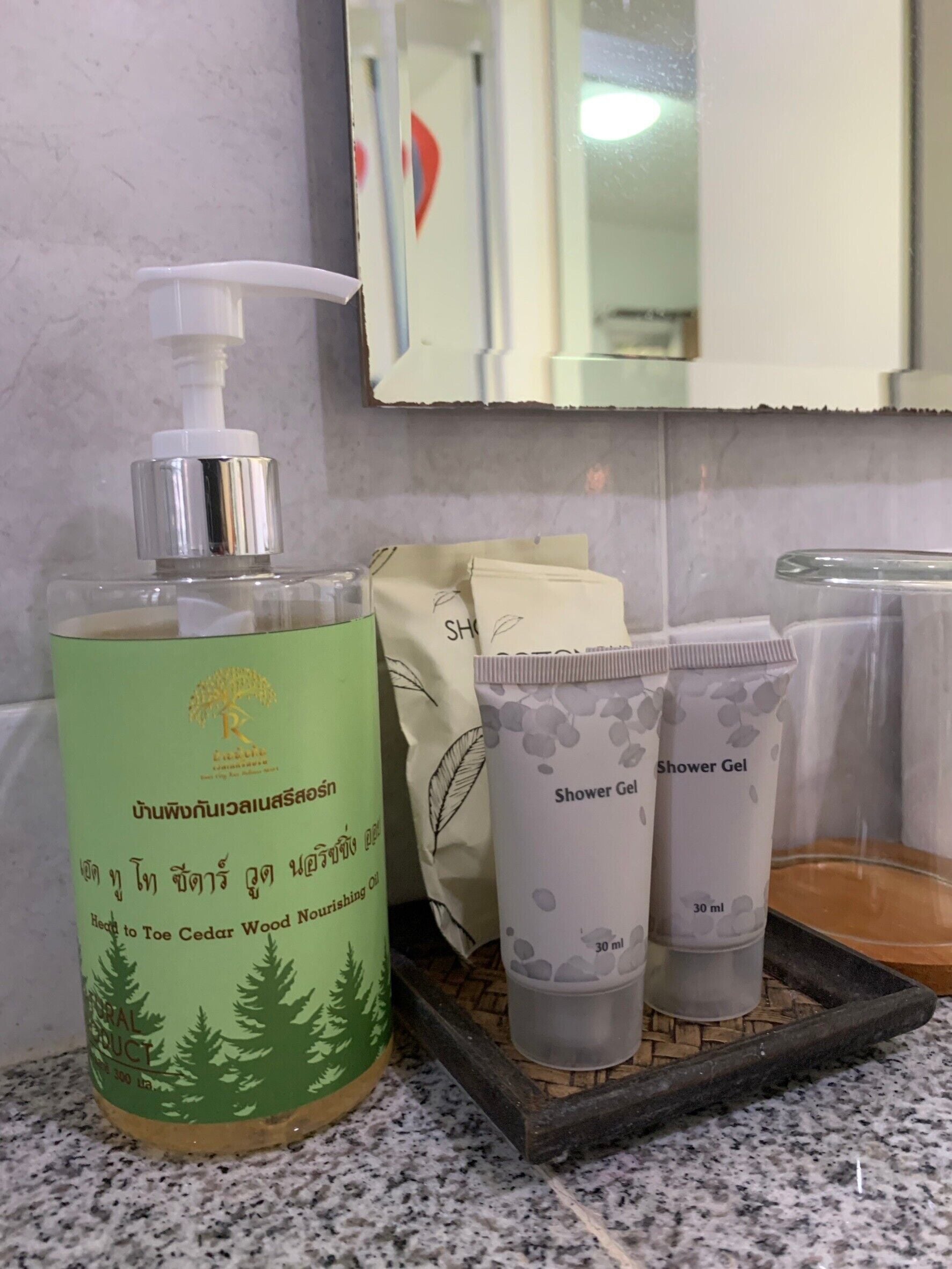 A bathroom with a bottle of Cedar Wood Nourishing Oil, a shower gel, and a soap dispenser on a tray.