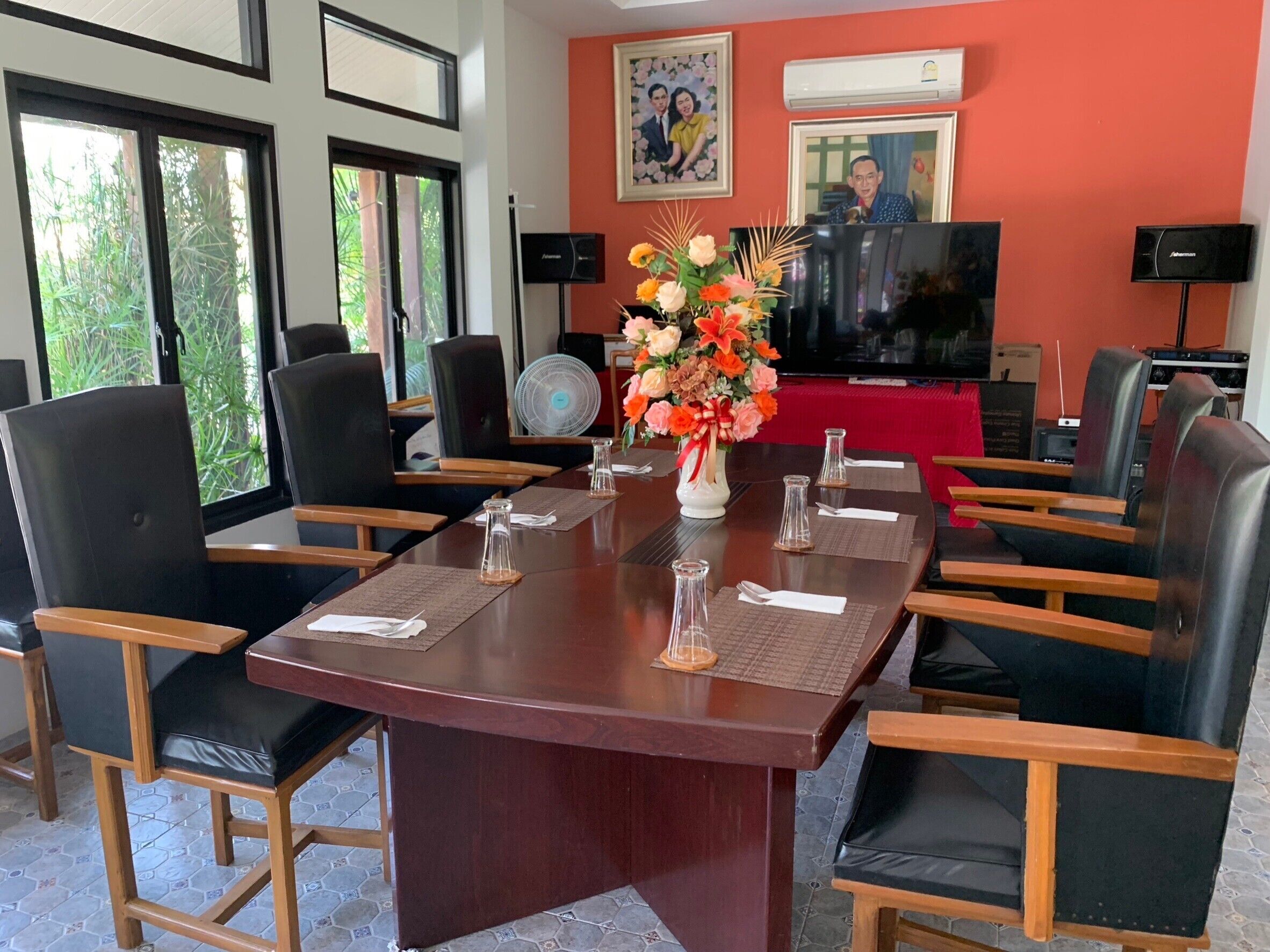 Un salón de conferencias con una gran mesa, sillas, un televisor y una decoración floral.