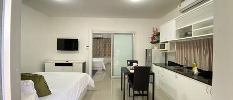 A modern hotel room with a bed, a desk, a dining area, and a kitchenette.