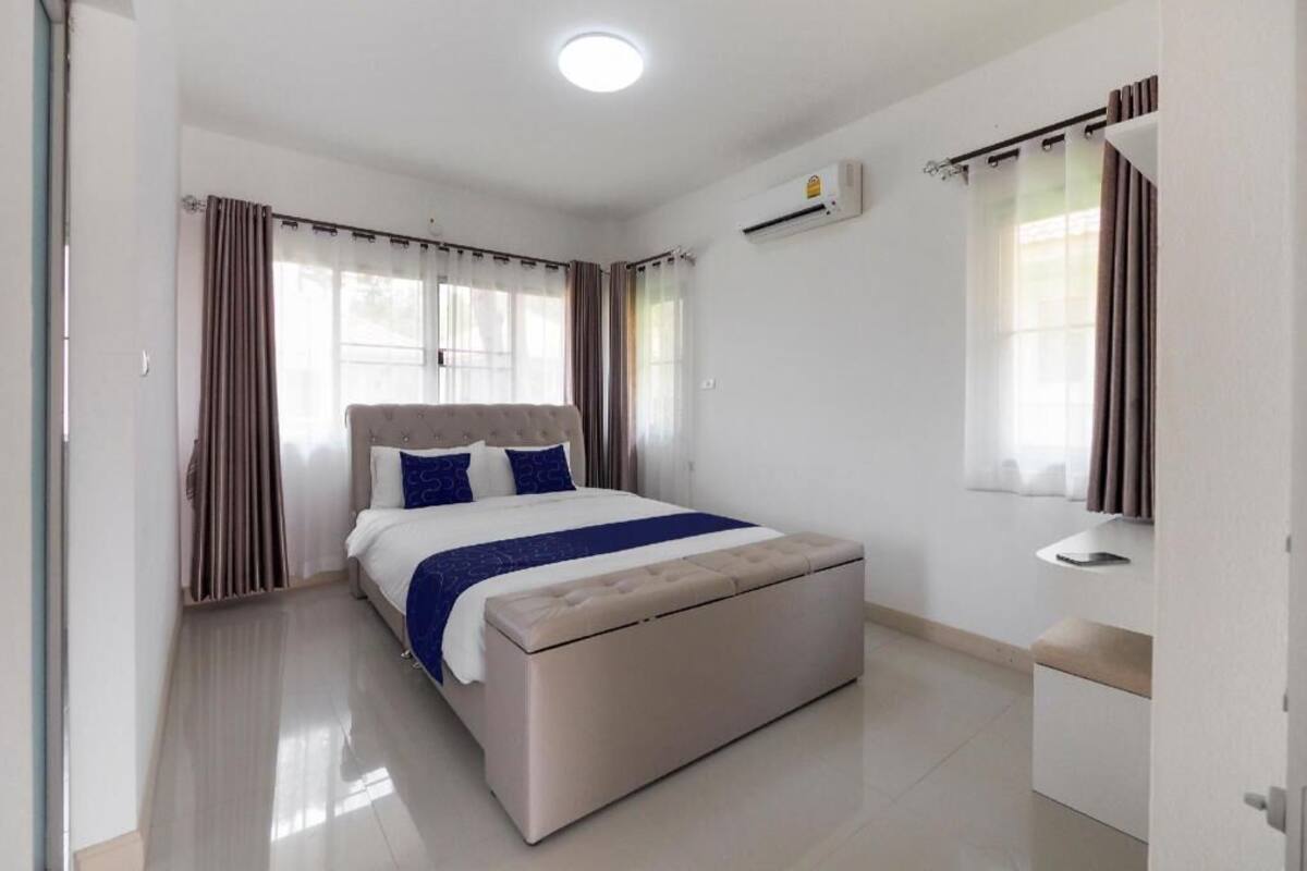 A bedroom with a bed, curtains, an air conditioning unit, and a bedside table.
