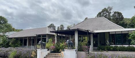 Un bâtiment moderne doté d’un patio couvert, de deux statues d’éléphants et d’un jardin agrémenté de fleurs violettes.