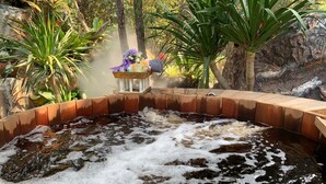 A hot tub surrounded by plants and a wooden deck. - Baan Pingkan Wellness Resort (San Kamphaeng)