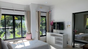 A bedroom with a bed, a TV, a desk, and a window with curtains. - Baan Pingkan Wellness Resort (San Kamphaeng)