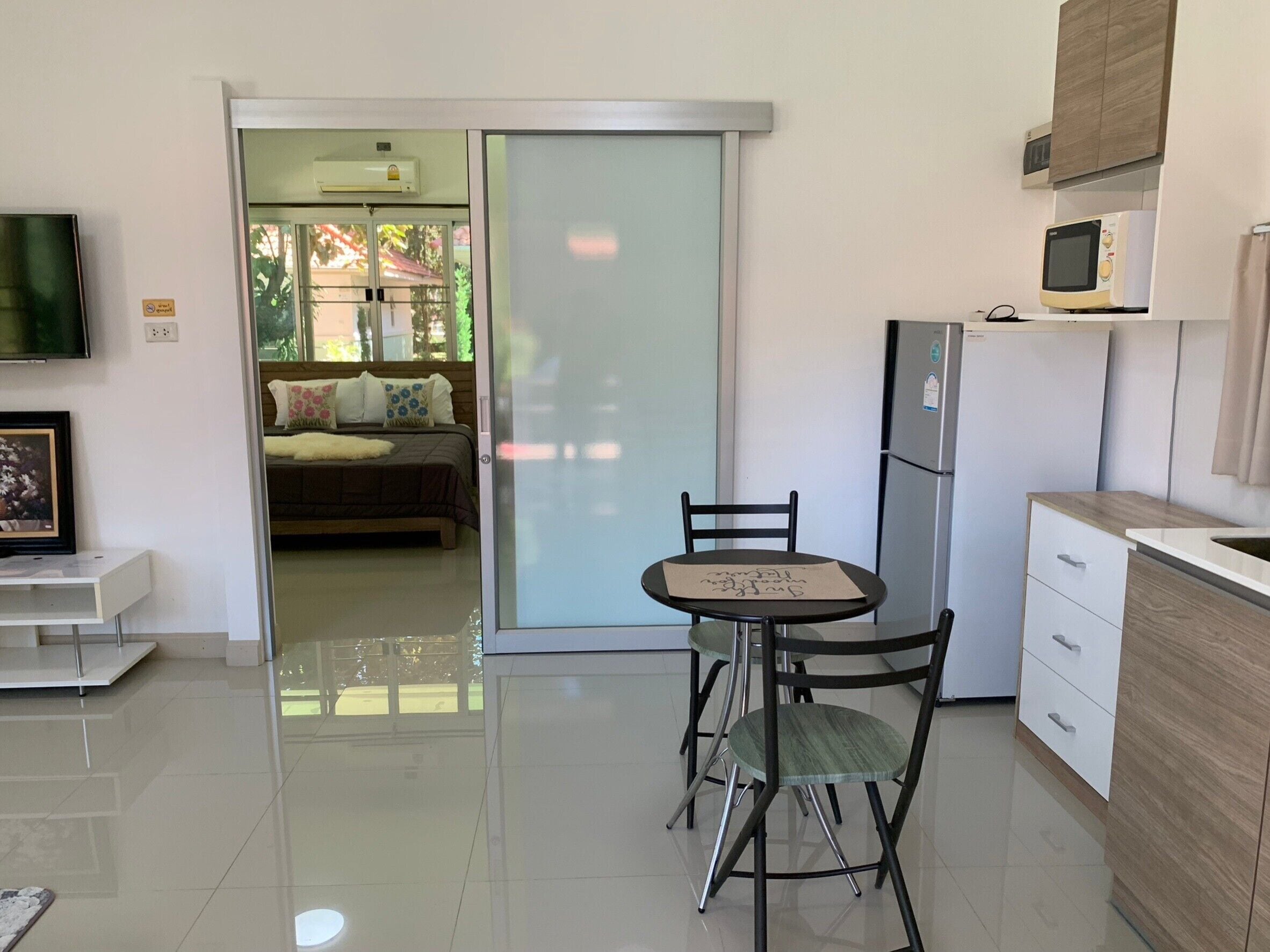 Una cocina moderna con comedor, televisor montado en la pared y puerta corrediza de vidrio que da a un dormitorio.