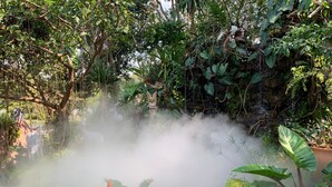 A misty garden with a stone structure, lush greenery, and a waterfall. - Baan Pingkan Wellness Resort (San Kamphaeng)