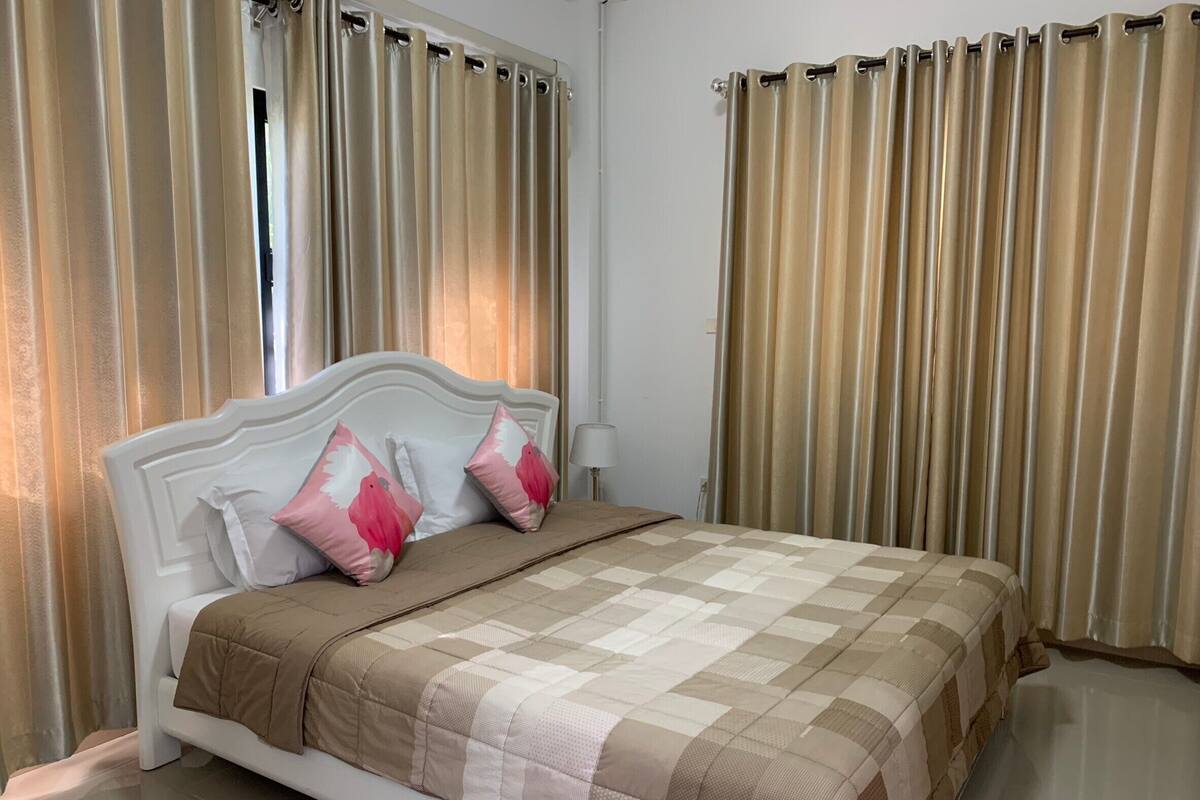 A neatly made bed with a checkered bedspread, two pillows with a bird design, and a white headboard.