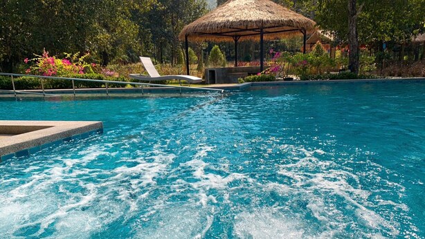 A swimming pool with a hot tub area, surrounded by lush greenery and a thatched-roof structure. - Baan Pingkan Wellness Resort (San Kamphaeng)