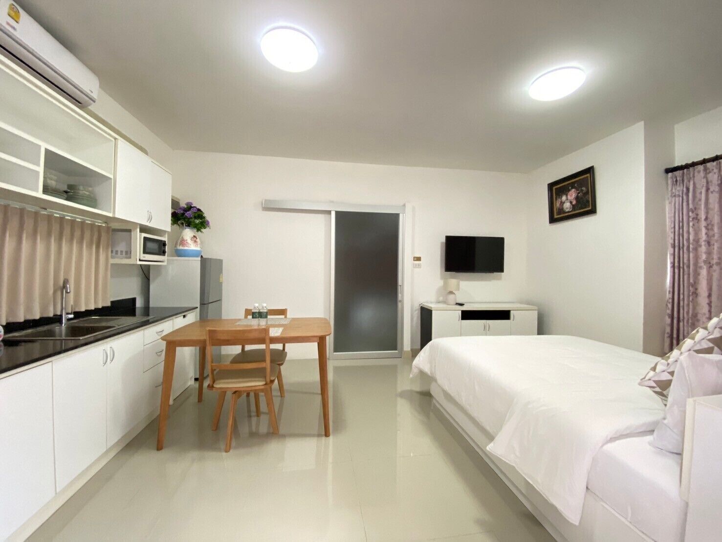 A compact hotel room with a kitchenette, a dining area, a bed, and a TV.