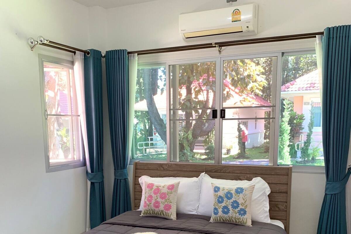 A bedroom with a bed, a window, curtains, and an air conditioning unit.