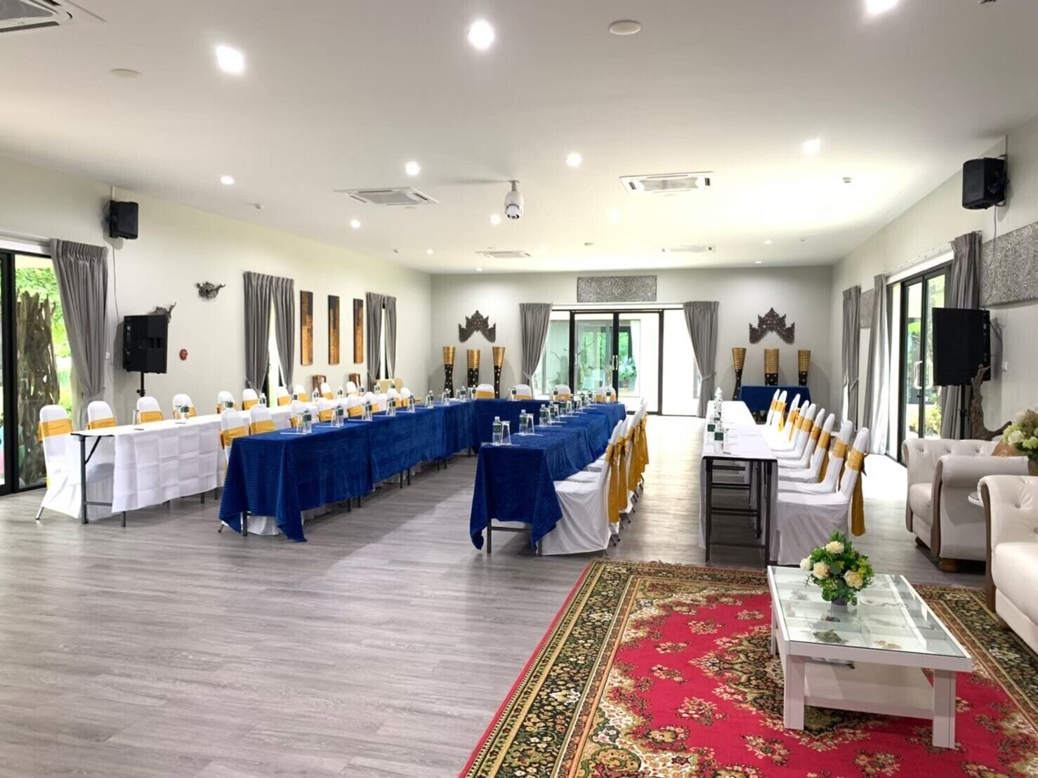 A conference room with long tables, white chairs with yellow sashes, and a red patterned carpet.