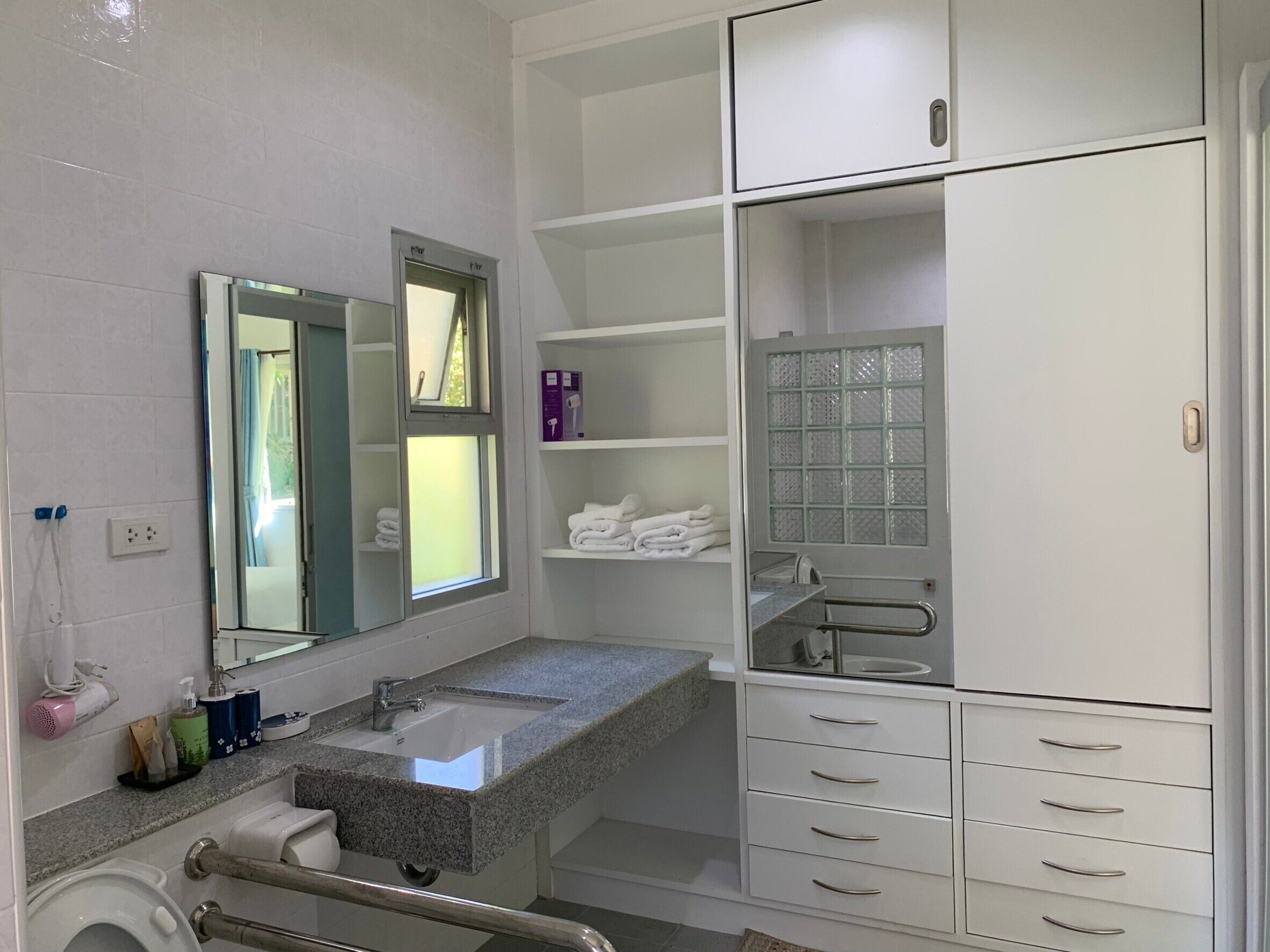 A modern bathroom with a granite countertop sink, a mirror, a window, and a walk-in shower.