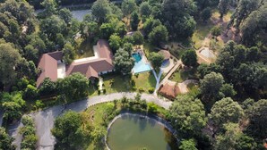 An aerial view of a residential area with a swimming pool, a pond, and a road. - Baan Pingkan Wellness Resort (San Kamphaeng)