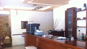 Una cocina con una barra de madera, taburetes, una cafetera y un mueble con botellas.