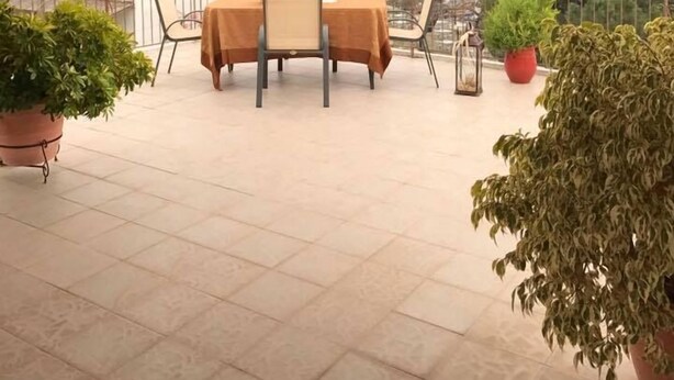 Un patio al aire libre con techo de madera, una mesa con sillas, plantas en macetas y vistas a un cuerpo de agua y montañas a lo lejos.