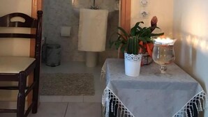 Una habitación pequeña y acogedora con una silla de madera, una mesa con mantel de encaje, una planta en maceta y una vela.