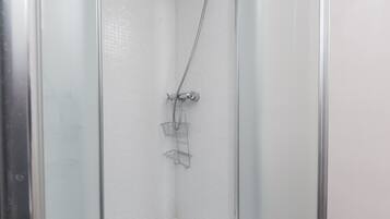 Une douche avec une porte en verre, un pommeau de douche en métal et une étagère en métal.